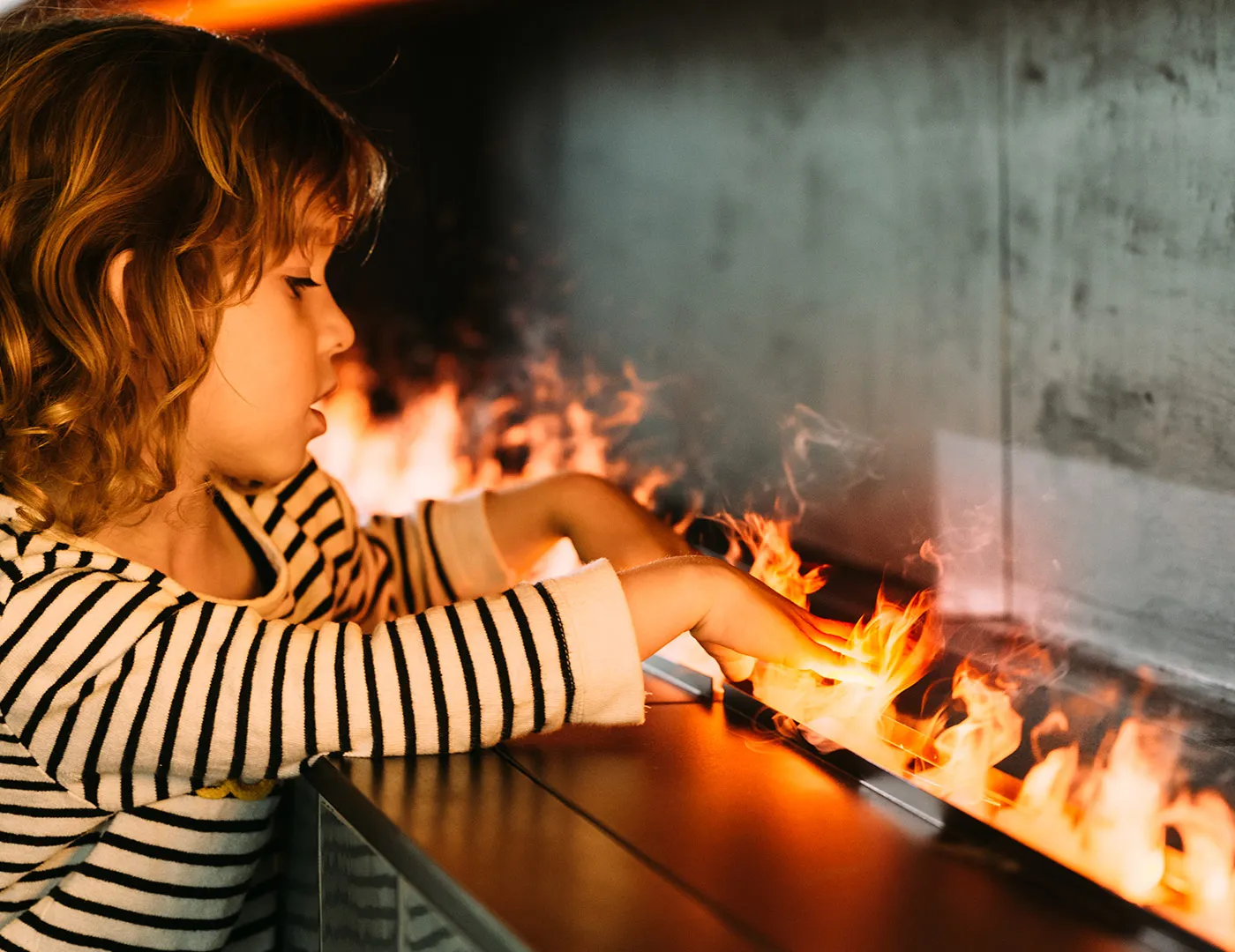 Little girl with her fingers sticking into a water vapour fireplace flame
